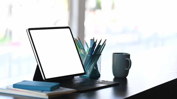 Side view of creative designer workspace with a tablet computer, stationery, notebook and coffee cup  on white table.