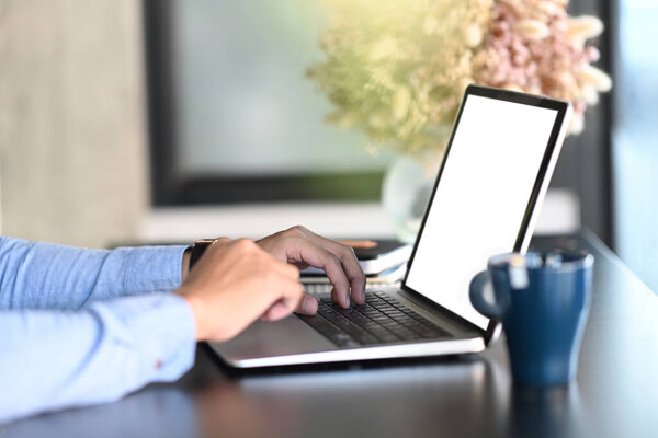 Side view man hands typing on keyboard of mock up laptop computer with blank screen.