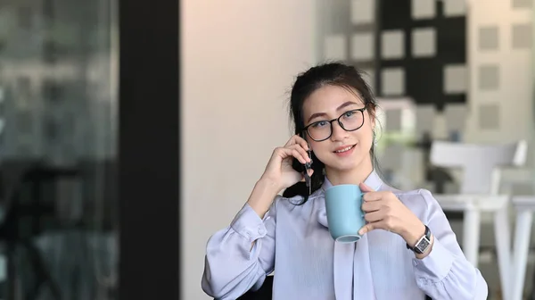 魅力的な若い女性がコーヒーを飲み オフィスで携帯電話で話す姿 — ストック写真