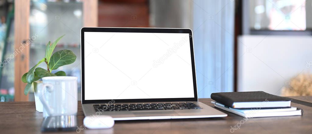 An open computer laptop, coffee cup, notebook and plant on wooden table. Blank screen monitor for graphic display montage.