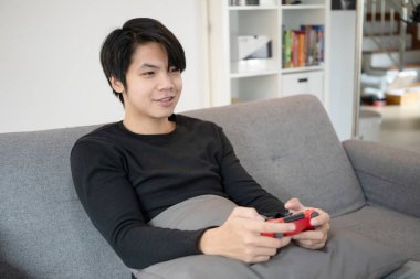 Kanepede video oyunu oynayan mutlu Asyalı genç adam..