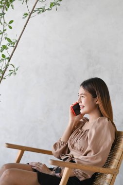 Kafede oturup cep telefonuyla konuşan mutlu genç bir kadının portresi..