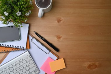Akıllı telefon, defter, yapışkan not ve ahşap masa üzerindeki kahve fincanı ile basit çalışma alanının yüksek açılı görüntüsü.