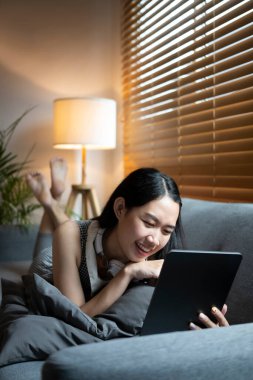 Rahat koltukta uzanan ve dijital tablet kullanan sıradan bir kadın..