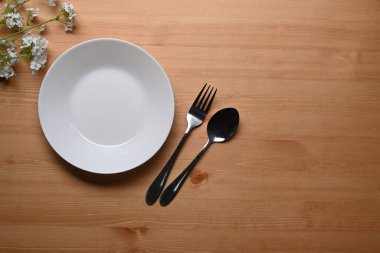 Ahşap zemin üzerinde seramik tabağın, kaşığın ve çatalın üstünde.