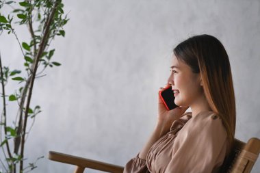 Gülümseyen ve cep telefonuyla konuşan mutlu genç bayanın yan görüntüsü.