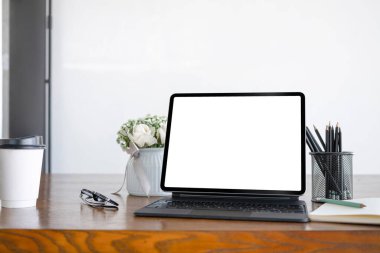 Kablosuz klavyeli dijital tableti, kahve fincanını ve ofis malzemelerini ahşap masada kapat.