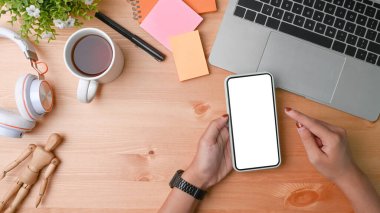 Ahşap masada boş ekranı olan akıllı telefonu tutan kadın..