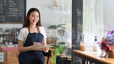 Önlüklü arkadaş canlısı garson ve kahve dükkanında duruyor..