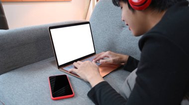 Kesilmiş çekim, gülümseyen genç adam kanepede yatıyor ve internette dizüstü bilgisayarla sörf yapıyor..