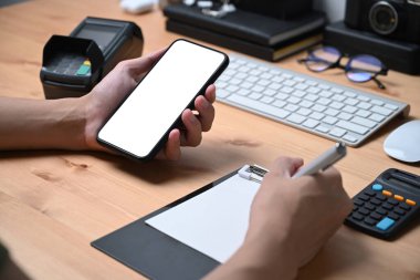 İş adamı cep telefonu bilgilerini kontrol ediyor ve not defterine not alıyor..