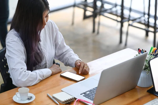 アジアの女性従業員がノートパソコンで作業し オフィスで携帯電話で情報を検索 — ストック写真