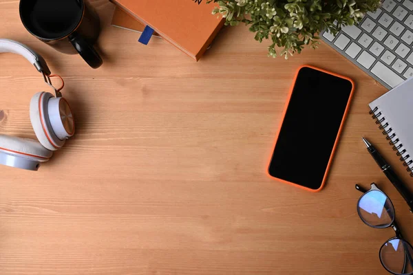 Mobile phone, headphone, notebook, glasses, coffee cup and houseplant on wooden background.