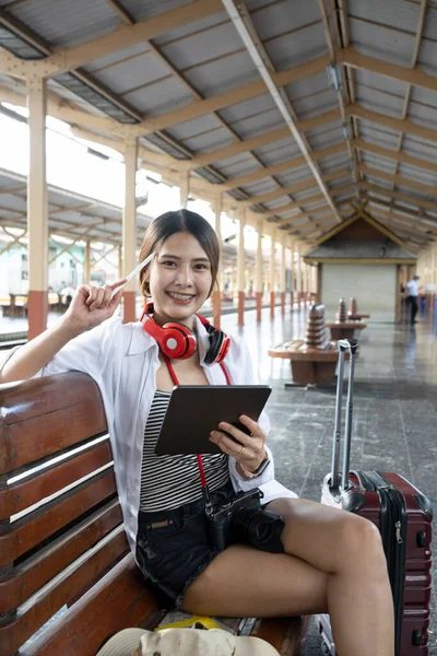 Happy female using digital tablet during waiting for train at the railway station.