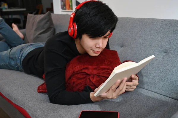 Mladý Muž Sluchátkách Ležící Pohovce Čtení Knihy — Stock fotografie