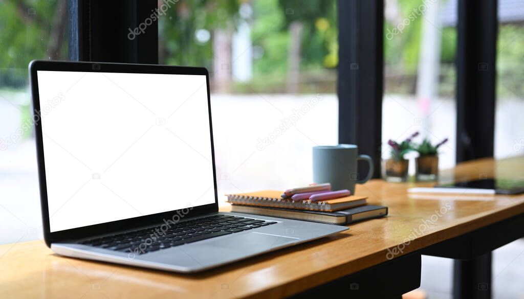 Close up view mock up laptop with empty screen, books and coffee cup on wooden table.