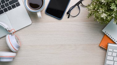 Laptop bilgisayarı, cep telefonu, kulaklık, gözlük, ahşap masadaki bir defter..