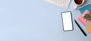 Akıllı telefon, yapışkan not, kahve fincanı ve mavi arka planda not defteri olan üst görünüm yaratıcı çalışma alanı.