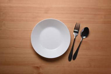 Seramik bir tabak, tahta arka planda kaşık ve çatal..