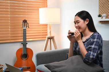 Oturma odasındaki kanepede oturmuş kahve içen huzurlu genç bir bayan..