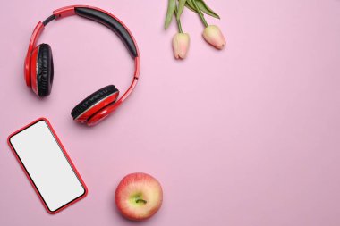 Pembe arka planda cep telefonu, kulaklık, elma ve pembe laleler..