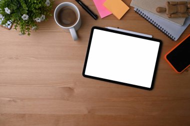 Üst görünüm dijital tablet, akıllı telefon, kahve fincanı, ev bitkisi ve tahta zemin üzerindeki defter.