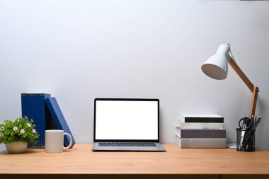 Öndeki dizüstü bilgisayar, kitaplar, lamba, kahve fincanı ahşap masadaki bir bitki..