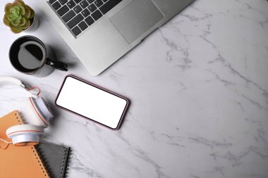 Üst görünüm akıllı telefon, kulaklık, not defteri ve klavye mermer arka planda.