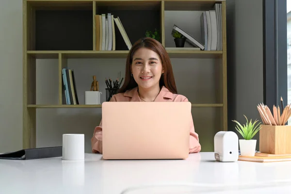 若い女性デザイナー彼女のラップトップコンピュータとオフィスに座って カメラに笑みを浮かべて — ストック写真