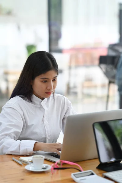 若いアジアの女性のオフィスワーカーは 彼女のオフィスデスクでラップトップコンピュータで作業に集中します — ストック写真