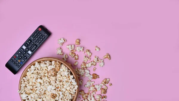 带爆米花的木制碗和粉色背景的遥控器 — 图库照片