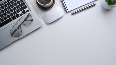 Üst görünüm dizüstü bilgisayar, gözlük, defter ve gözlükler beyaz ofis masasında..