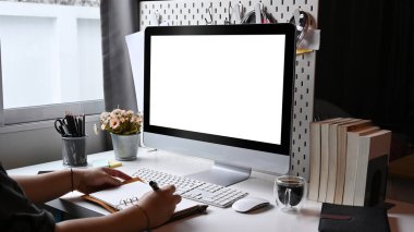 Bilgisayarın önünde oturan ve deftere not alan bir adam..