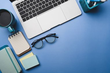 Dizüstü bilgisayarı, bardakları, kahve fincanı ve defteri olan şık çalışma alanı.