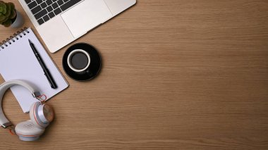 Üst düzey kahve fincanı, kulaklık, defter ve dizüstü bilgisayar ahşap masada..