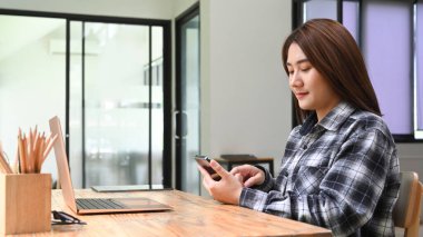 Genç bir kadın ofisinde oturuyor ve cep telefonu kullanıyor..