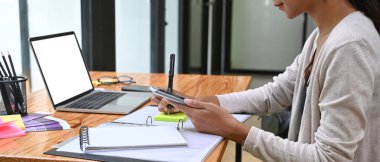 Kırpılmış kadın tasarımcı cep telefonu kullanıyor ve deftere not alıyor..