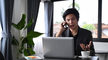 İş adamı iş ortağıyla cep telefonuyla konuşuyor ve laptopla çalışıyor..
