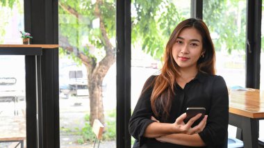 Asyalı kadın işyerinde oturuyor ve kameraya gülümsüyor..