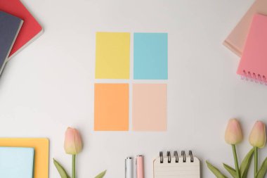 Renkli yapışkan notlar, pembe laleler ve beyaz arka planda not defteri..