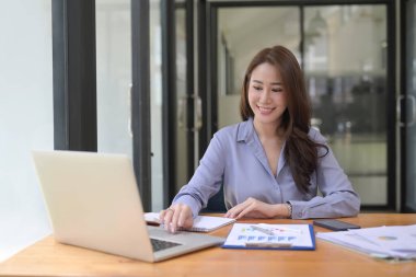 Dizüstü bilgisayarla çalışan ve ofiste mali raporları okuyan çekici bir iş kadını..