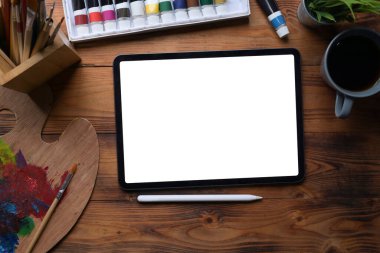 En iyi görüntü sanatçısı çalışma alanı dijital tablet, boya fırçaları, palet, suluboya ve kahve fincanı ahşap masa üzerinde.