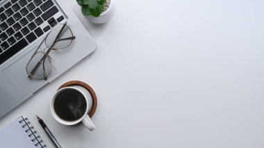 Dizüstü bilgisayarı, kahve fincanı ve defteri olan beyaz ofis masası..