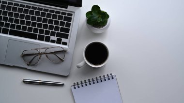 Bilgisayar laptopu, gözlük, kahve fincanı ve defter beyaz ofis masasında..
