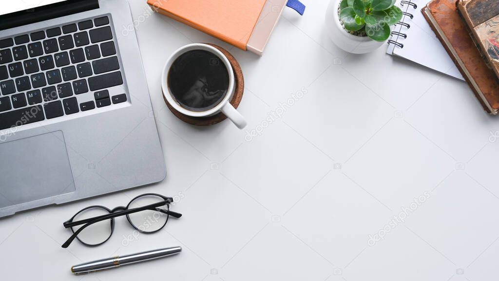 Top view white office desk with laptop computer, coffee cup and glasses.