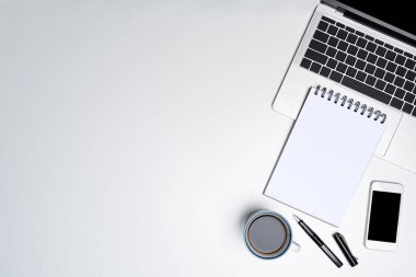Boş defter, dizüstü bilgisayar ve akıllı telefon beyaz ofis masasında..