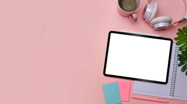 Üst görünüm dijital tablet, defter, yapışkan not ve kahve fincanını pembe arka planda oluşturur..