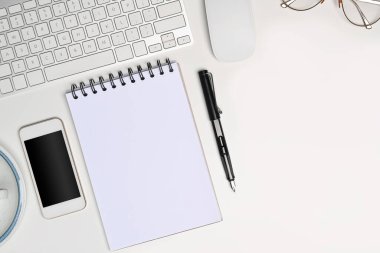 Boş defter, akıllı telefon, gözlük ve kalemle beyaz ofis masasının üstünde..