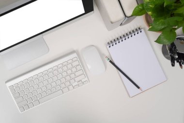 Beyaz masa üzerinde bilgisayar, defter ve ev bitkisi olan modern iş yeri.