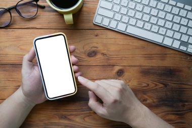 Yukarıda genç adam ahşap masada akıllı telefon kullanıyor..
